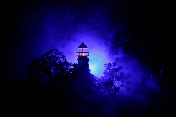 Маяк со световым лучом ночью с туманом. Старый маяк стоит на горе. Украшение стола. Селективный фокус
 - Фото, изображение