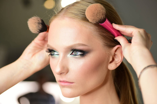 Beauty model with glamour look, hairstyle. Woman with makeup face hold brushes at head. Woman with blond hair and makeup brushes, beauty. Girl with young skin face, skincare, youth. - Фото, изображение