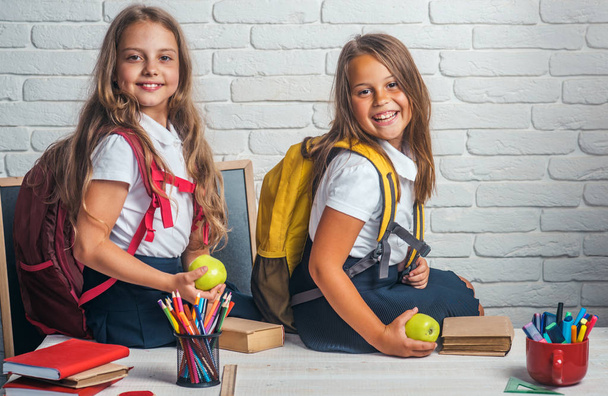 School time of girls. Friendship of small sisters in classroom at knowledge day. Back to school and home schooling. Little girls eat apple at lunch break. Happy school kids at lesson in september 1 - Foto, Imagem