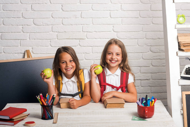 Little girls eat apple at lunch break. Friendship of small sisters in classroom at knowledge day. School time of girls. Happy school kids at lesson in september 1. Back to school and home schooling - Φωτογραφία, εικόνα