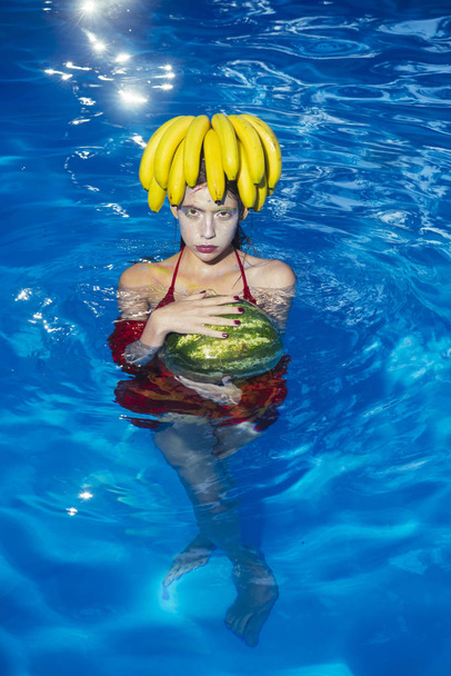 girl with tropical fruit in pool. girl swim with watermelon and banana in water - Foto, Imagem