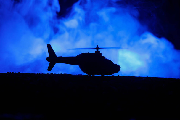 Silhouette of military helicopter ready to fly from conflict zone. Decorated night footage with helicopter starting in desert with foggy toned backlit. Selective focus. - Foto, Imagen
