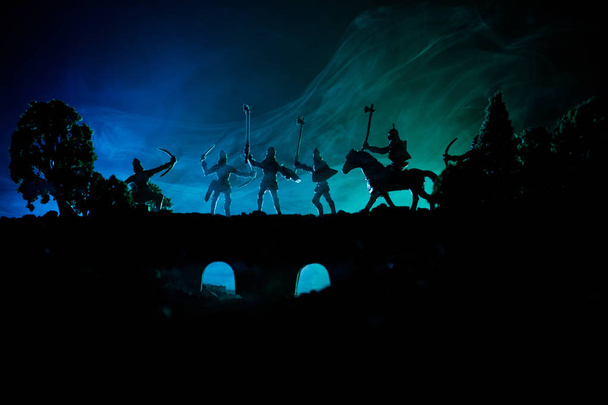 Средневековая боевая сцена на мосту с кавалерией и пехотой. Силуэты фигур как отдельные объекты, борьба между воинами на темном, тонированном туманном фоне. Ночная сцена
. - Фото, изображение