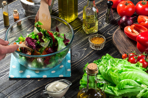 Mies valmistaa salaattia tuoreilla vihanneksilla puupöydällä. Ruoanlaitto maukasta ja terveellistä ruokaa. lähikuva
 - Valokuva, kuva