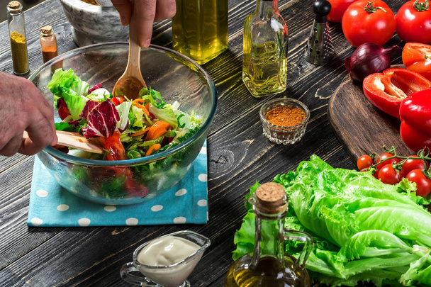 Az ember, egy fából készült asztal friss zöldség saláta készítése. Főzés ízletes és egészséges ételeket. Közeli kép: - Fotó, kép