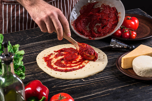 Une purée de tomate à la main masculine sur une base de pizza avec cuillère sur un vieux fond en bois
 - Photo, image