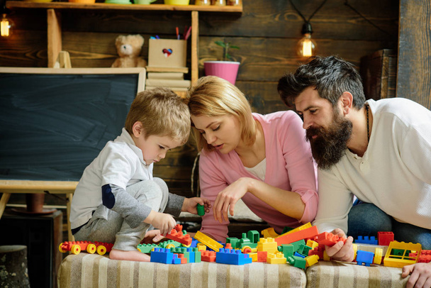 Father, mother and cute son play with constructor bricks. Kid with parents play with plastic blocks, build construction. Family on busy face spend time together in playroom. Caring parents concept. - Valokuva, kuva