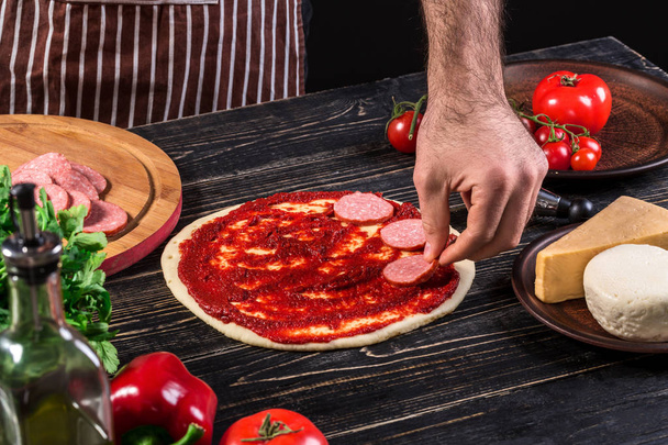 Aşçı mutfakta, pizzanın malzemelerini koyuyor. Pizza konsepti. Gıda üretimi ve teslimatı. - Fotoğraf, Görsel