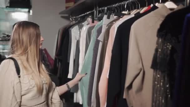 Blonde fille est à la recherche de vêtements sur cintres dans la boutique à la mode
 - Séquence, vidéo