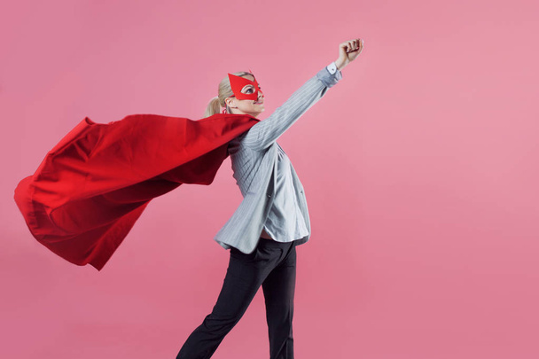 Young attractive woman superhero. Girl in a business suit and a mask with red cloak of hero. - Photo, Image