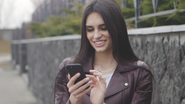 Portret van een brunette vrouw lachend en met behulp van een smartphone die buiten op straat. - Video