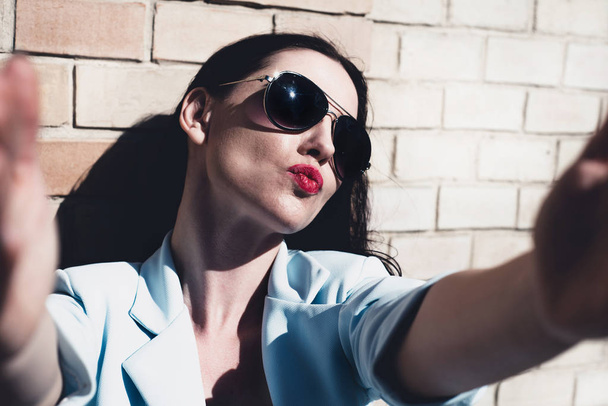 Divatos és modern nő vesz egy selfie. Szép és vonzó nő egy kék blézer és napszemüveg csinál kifolyó kamera, selfie. Retro vintage stílusú. - Fotó, kép