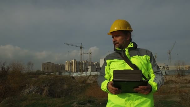 dojrzały mężczyzna robotnik majster w hełm z tabletem na tle budowy - Materiał filmowy, wideo