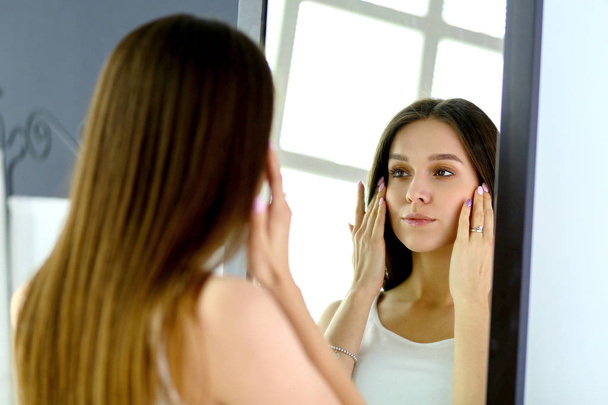Young woman looking herself reflection in mirror at home - Foto, afbeelding