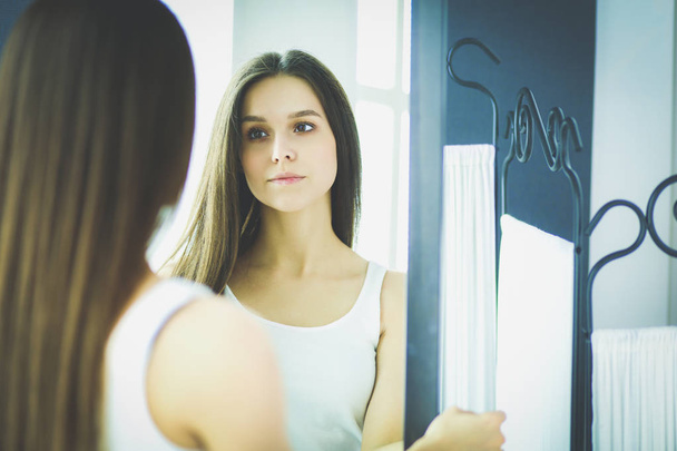Young woman looking herself reflection in mirror at home - Foto, Imagen