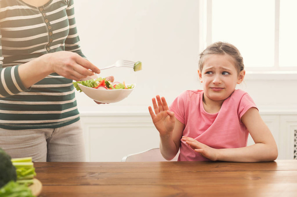 Mulher oferecendo sua salada filha, mas menina se recusando
 - Foto, Imagem