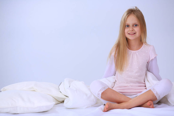 Little girl in the bedroom is sitting on the bed. Little girl is wearing a pajamas and sitting in bed . - Фото, зображення