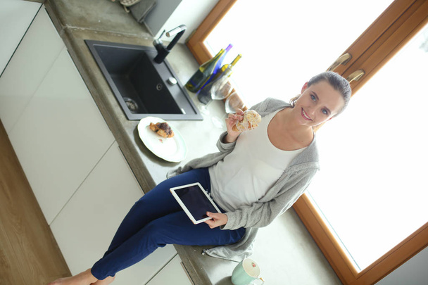 Beautiful young woman using a digital tablet in the kitchen. - Foto, Imagen
