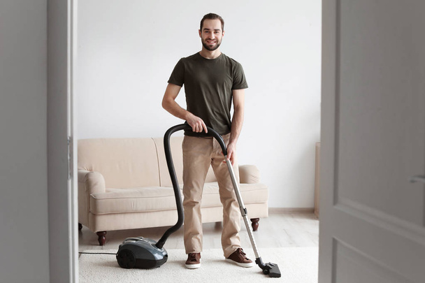 Young man cleaning carpet with vacuum in living room - Valokuva, kuva