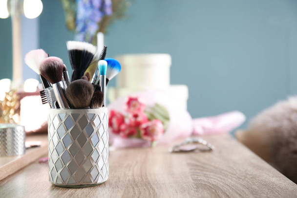 Holder with professional makeup brushes on wooden table - Photo, image
