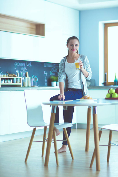 Mujer joven con jugo de naranja y tableta en la cocina. - Foto, imagen