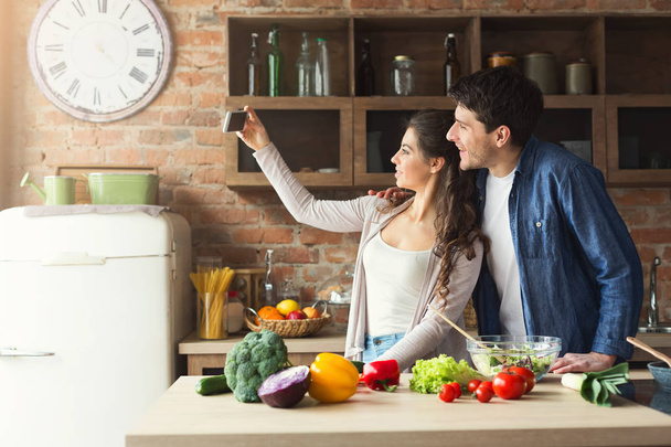 Happy couple cooking and taking selfie in kitchen - Photo, Image