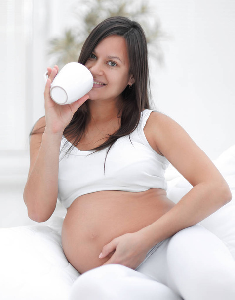 happy pregnant woman drinking milk sitting in the living room. - Фото, изображение