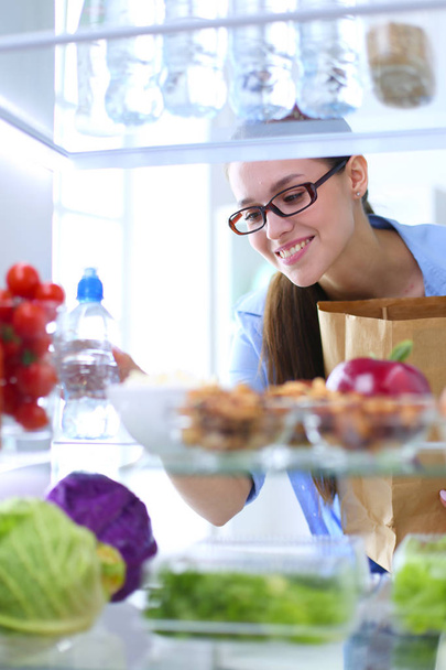 Sağlıklı yiyecek, sebze ve meyvelerle dolu açık buzdolabının yanında duran kadın portresi. - Fotoğraf, Görsel