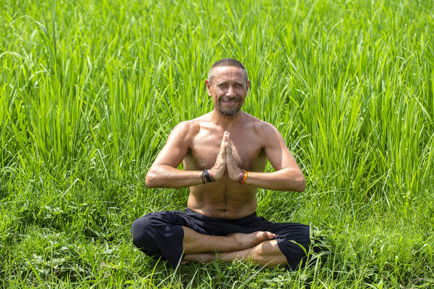 Man doing yoga and meditating in a position near a green rice terrace on the tropical island of Bali, Indonesia - Foto, Imagem