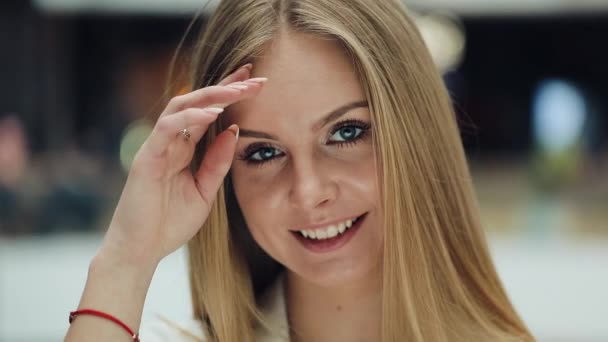 Smiling young blonde woman looks charming fixing her hair for a camera - Filmati, video