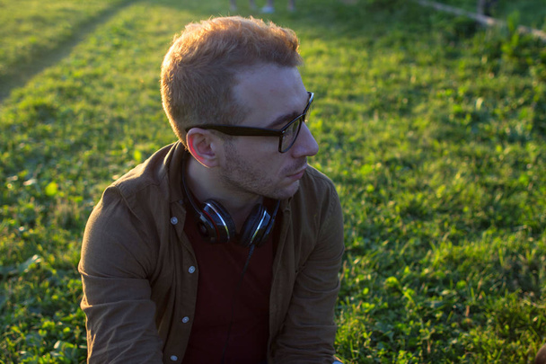 Side view of a young man in eyeglasses on green grass background. Guy portrait in sunset light. - Foto, immagini