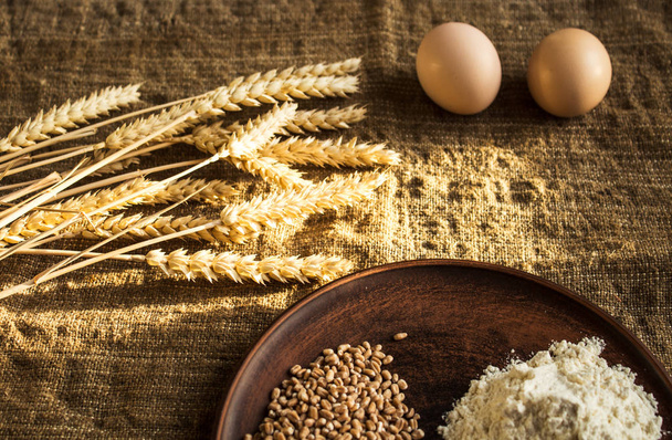 wheat flour eggs and spikelets of wheat on sackcloth background - Photo, Image