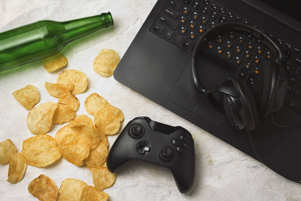 Ordenador portátil, Gamepad, Auriculares, Patatas fritas, Botella de cerveza en una l
 - Foto, imagen