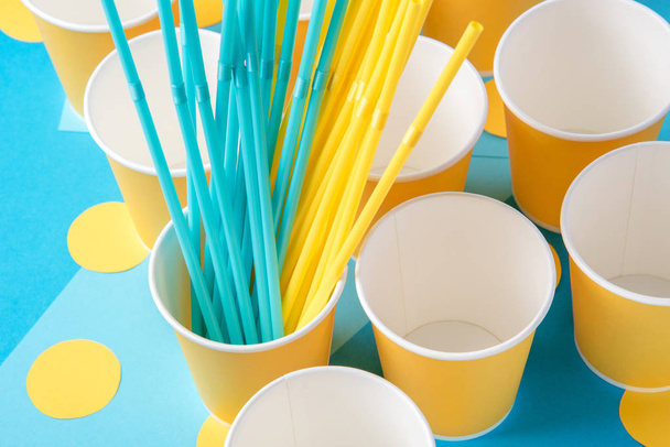 Желтые и голубые соломинки для вечеринки в бумажных стаканчиках на ярком пляже
 - Фото, изображение