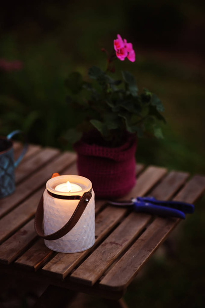 夜のキャンドル ライト、ポットとビンテージの水まき缶でゼラニウムの花で庭の夏シーン居心地の良い.  - 写真・画像