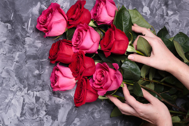 灰色のコンクリート背景に女性の手で新鮮な赤とピンクのバラの花束 - 写真・画像