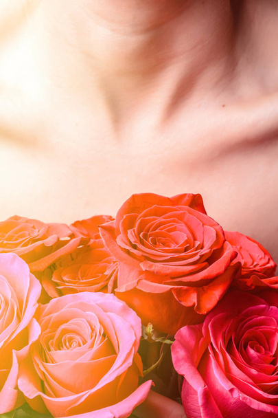Bouquet of bright fresh red and pink roses against the background of the female breast and collarbones - Photo, image