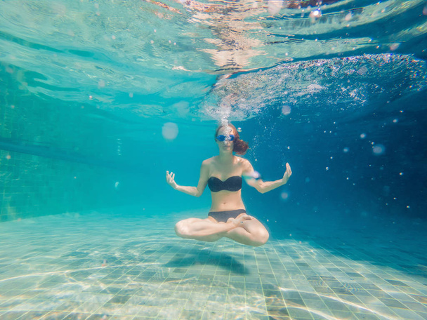 Young woman in black bikini in yoga position underwater in diving aquarium, full body shot, front view. - Fotoğraf, Görsel