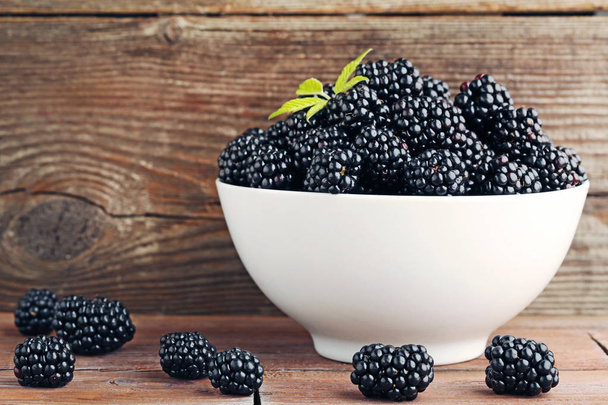 Ripe blackberries in bowl on wooden table - Foto, afbeelding