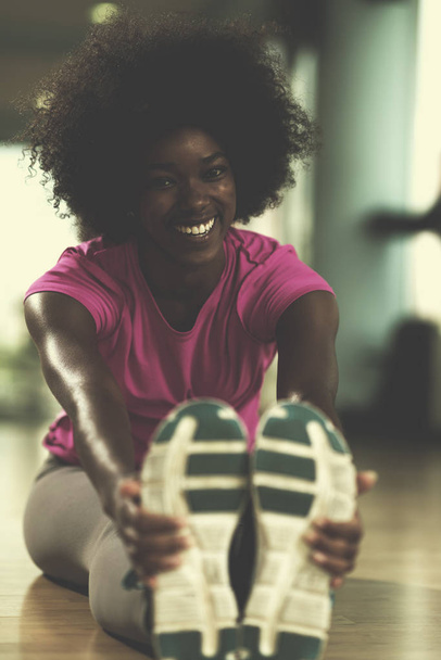 happy young african american woman in a gym stretching and warming up before workout - Fotó, kép