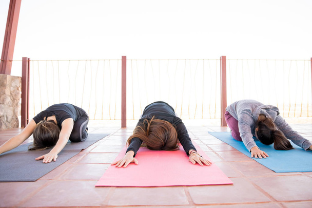Grupo de tres mujeres jóvenes sentadas en la esterilla de yoga y inclinadas hacia adelante con las manos extendidas en la clase de yoga
 - Foto, imagen