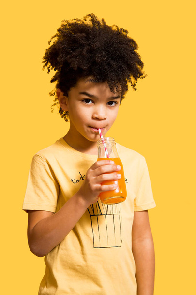 Cute little boy drinking orange juice with a straw - Fotó, kép
