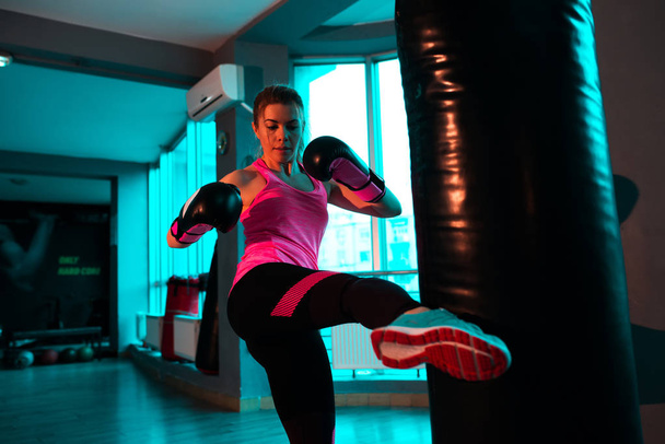 Blonde kickboxer woman foot kick into heavy bag in gym - Foto, afbeelding