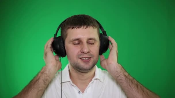 Een man in hoofdtelefoon luistert naar muziek op een groene achtergrond. - Video