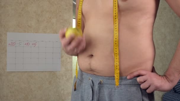 A fat man measures his waist, a big beer belly, a healthy lifestyle eating an apple - Footage, Video