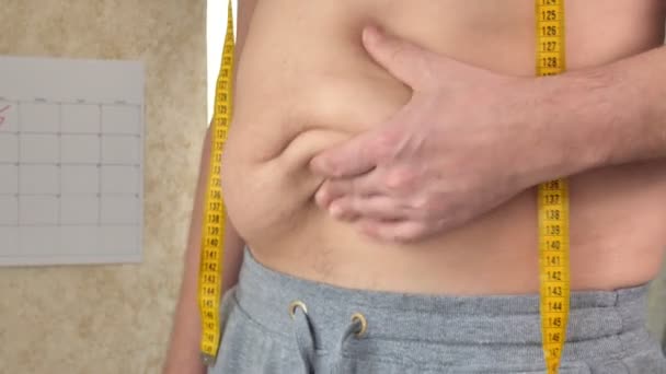 Толстяк измеряет свою талию, большой пивной живот, здоровый образ жизни поднимает жировые складки
 - Кадры, видео