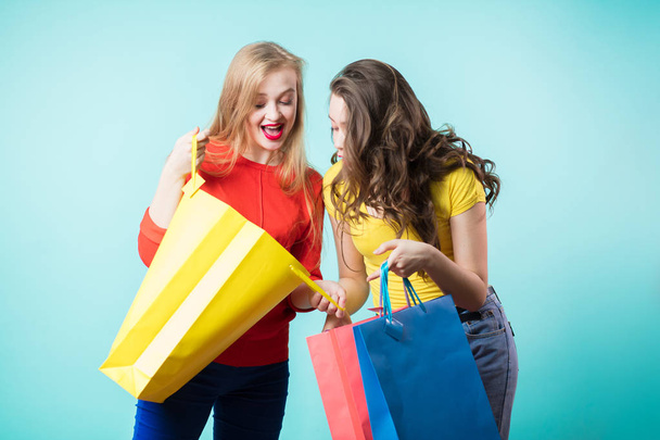 Two young joyful women with colorful shopping bags on blue background. - Foto, imagen