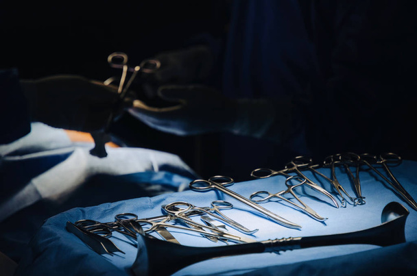 close up of surgical instrument lying on table while group of surgeon work in operation room at hospital, emergency case, surgery, medical technology, health care cancer and disease treatment concept - Foto, immagini