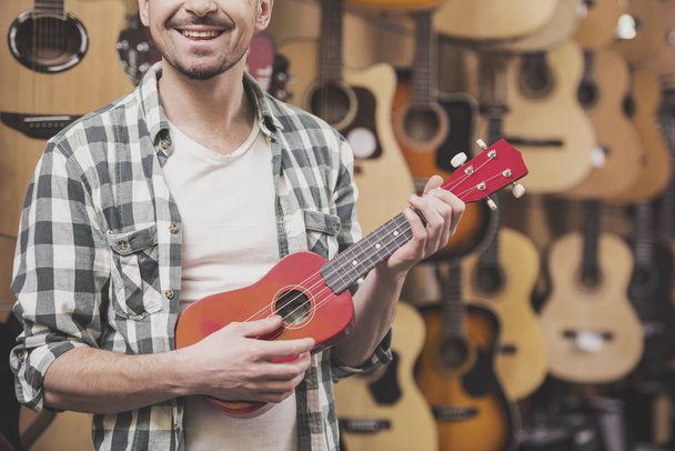Close-up. Man is holding red ukelele in music shop - Foto, Bild