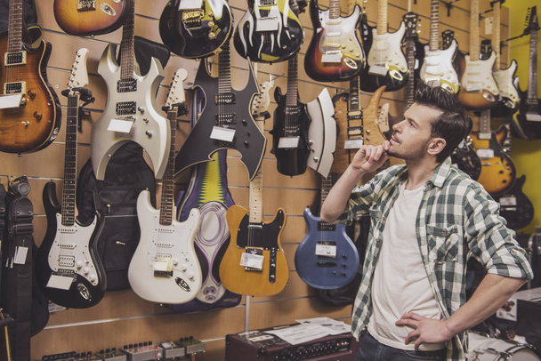 Young man is considering electric guitars music store - Zdjęcie, obraz